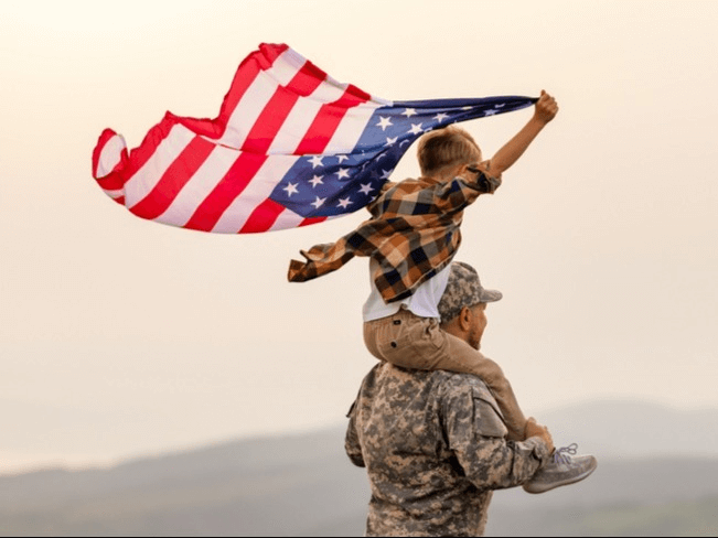Son on active military father's shoulder waving the American Flag