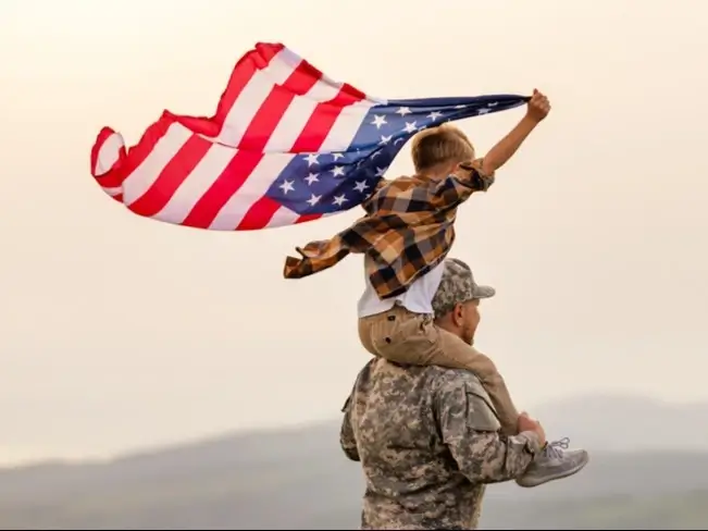Son on active military father's shoulder waving the American Flag